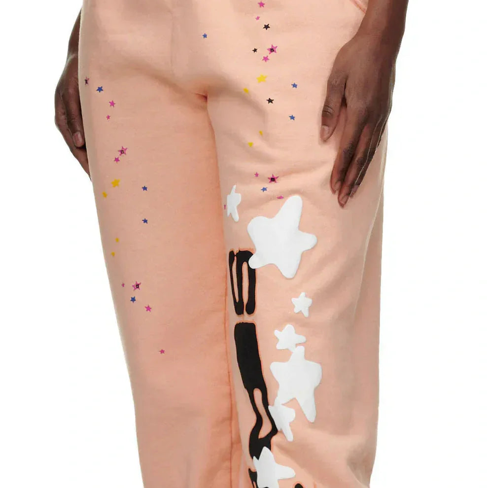 A person wearing light peach pants with white star patches, black abstract shapes, and small colorful star prints.