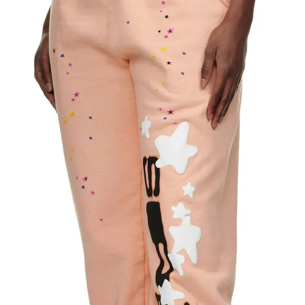 A person wearing light pink pants with multicolored star patterns and white star appliqués on the left leg.