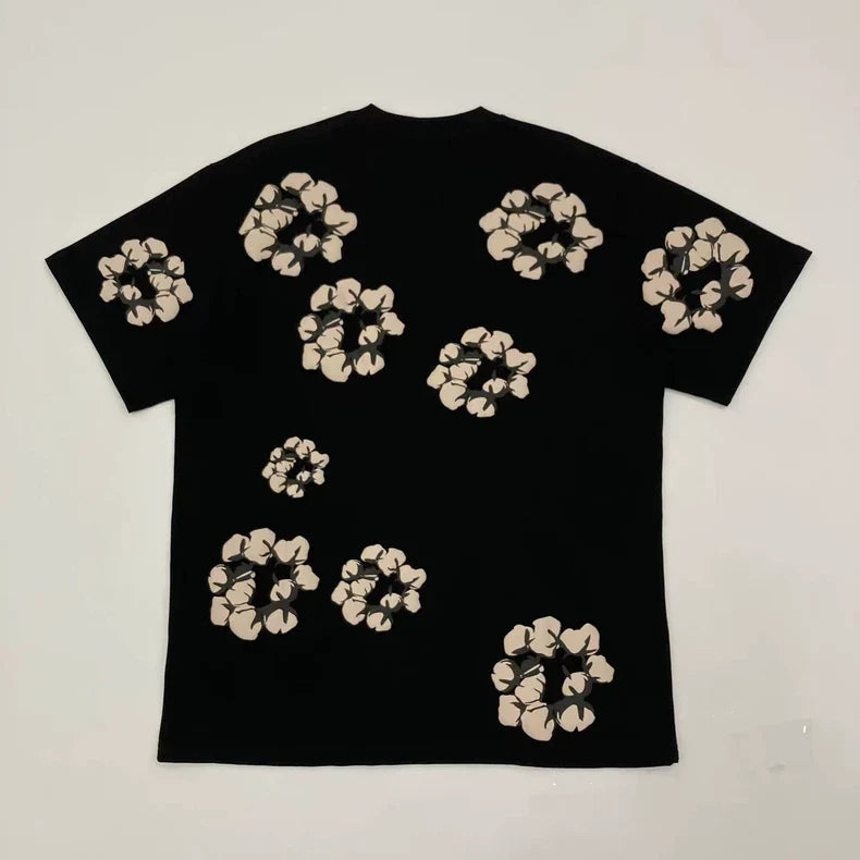 The Denim Tears Black Cotton Wreath Allover Print T-Shirt features beige abstract floral clusters of varying sizes scattered evenly across the back. The shirt is displayed flat on a white background.