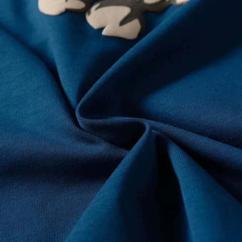 Close-up of the blue fabric of the Denim Tears Blue Cotton Wreath Allover Print T-Shirt, twisted into a swirl with part of its white and gray cotton wreath graphic visible near the top edge.