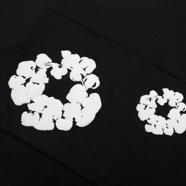 Two white floral ring prints evoke a cotton wreath on the black “Cotton Wreath” Denim Tears Hoodie, highlighting its distinctive black streetwear style.