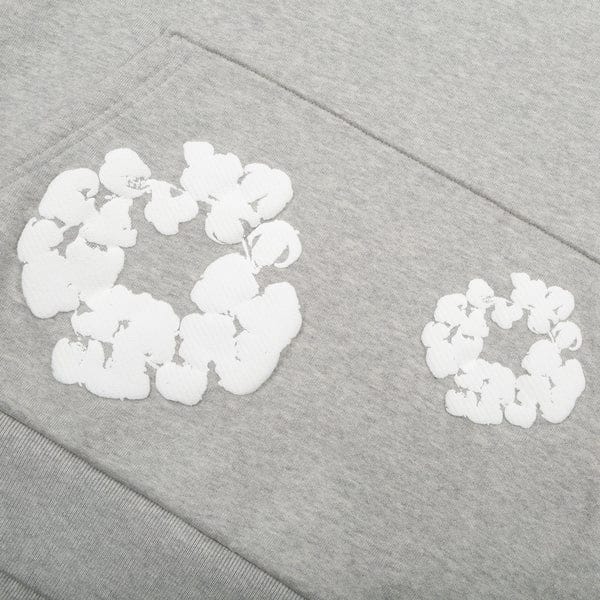 A close-up of the Gray “Cotton Wreath” Denim Tears Hoodie shows two white floral circle prints—resembling cotton wreaths—stitched on soft gray fabric, capturing subtle streetwear style in this pullover.