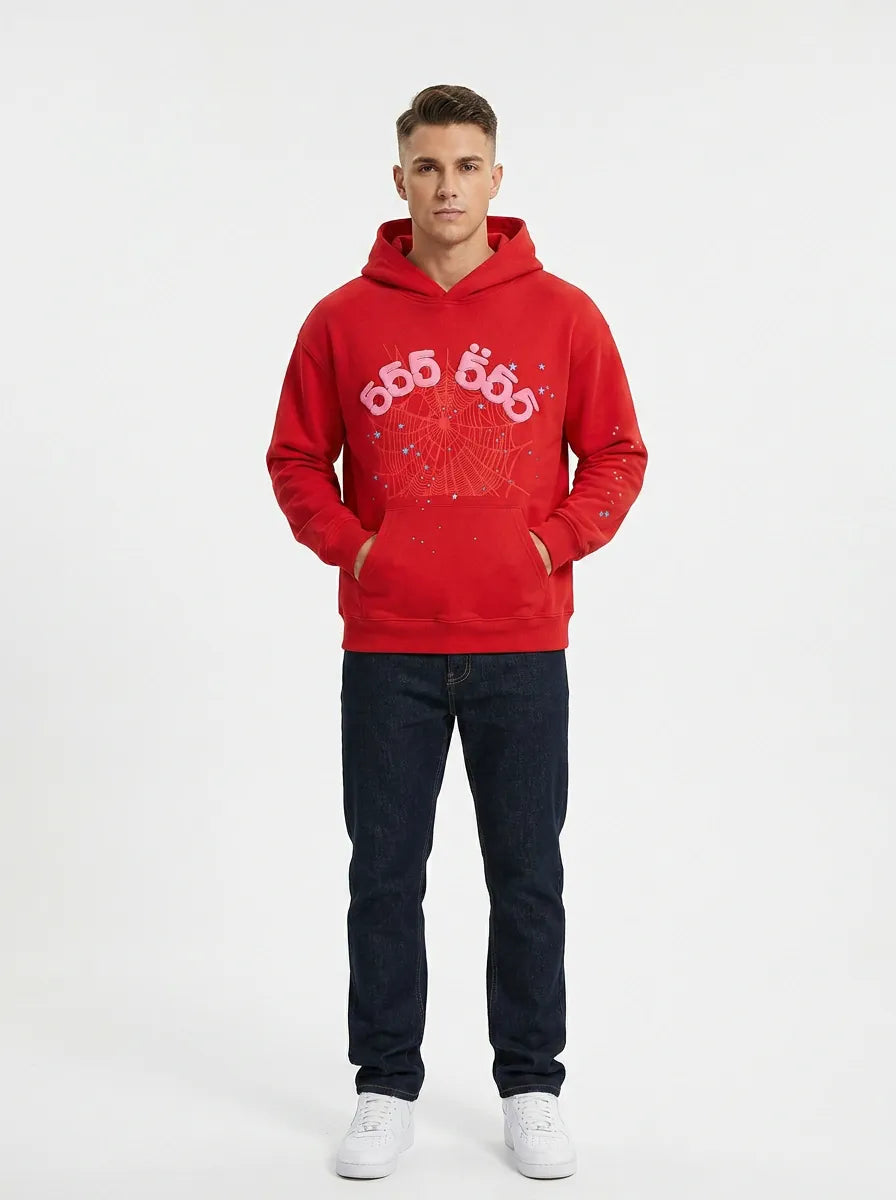 A man faces forward against a white background, wearing the Red 555 Sp5der Hoodie – 440GSM Heavyweight Sp5der 555 Web Oversized Pullover with dark jeans and white sneakers, embodying a streetwear vibe.