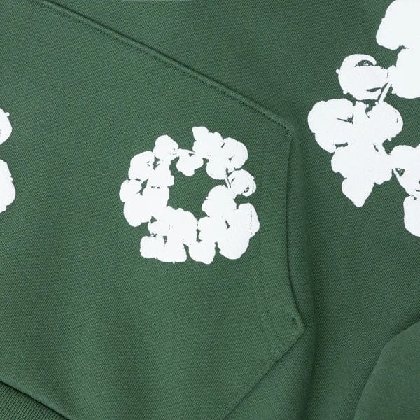 The Forest Green “Cotton Wreath” Denim Tears Hoodie is a streetwear pullover featuring a pocket and white floral print inspired by the Cotton Wreath motif.
