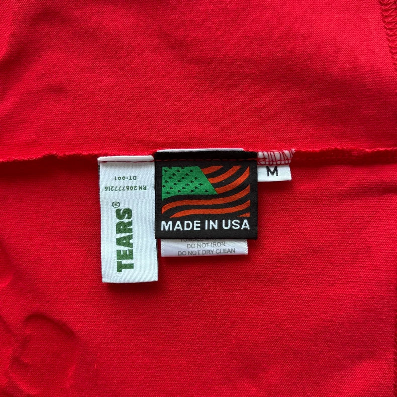 White tags on the Denim Tears Red Cotton Wreath Allover Print T-Shirt show TEARS?, a green and orange flag, MADE IN USA, care info, and an M tag for size medium.