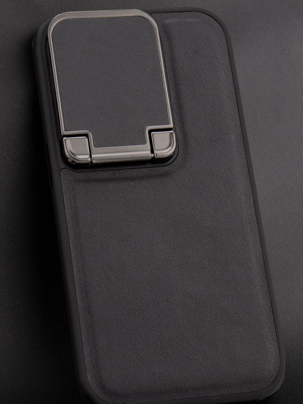 An iPhone 16 Pro Max Leather Case with a metal kickstand attached on the back, featuring a dual-layer shockproof TPU frame and camera shield, placed on a black surface.