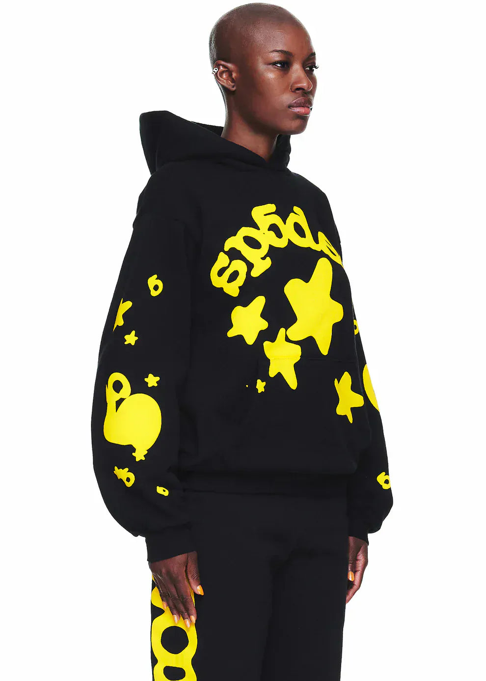 A person stands against a white background wearing the Black and Yellow Spider Hoodie with Star Lettering Print – a comfort-fit pullover featuring bold yellow star and abstract designs, perfect for everyday wear.