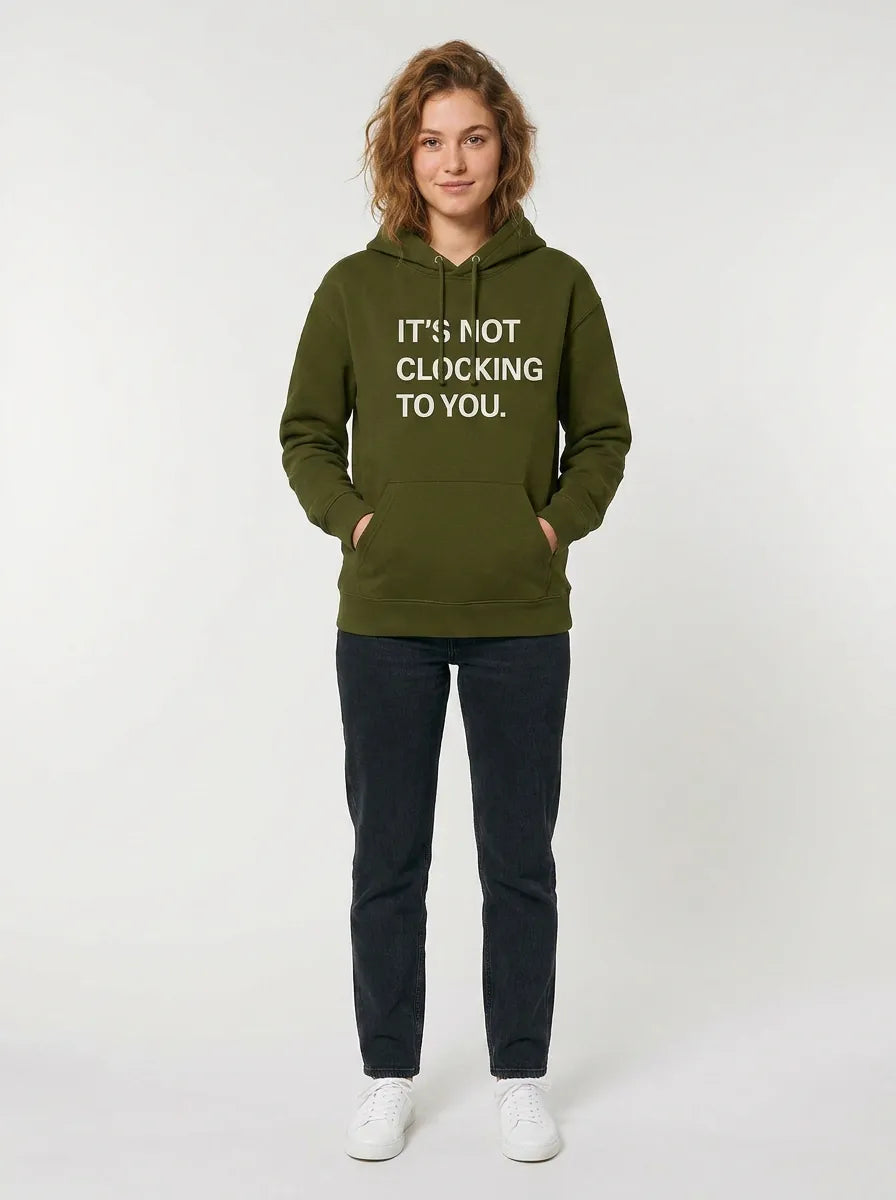 A person stands facing forward on a plain light background wearing the Its Not Clocking To You Hoodie—360GSM heavyweight 100% cotton graphic pullover hoodie in green—with black pants and white sneakers.