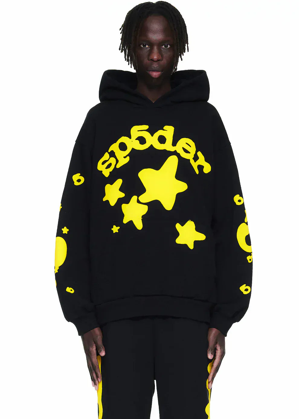 A person stands facing forward wearing the Black and Yellow Spider Hoodie  with Star Lettering Print— a comfort fit pullover hoodie for everyday wear, paired with matching pants featuring bold yellow stars.