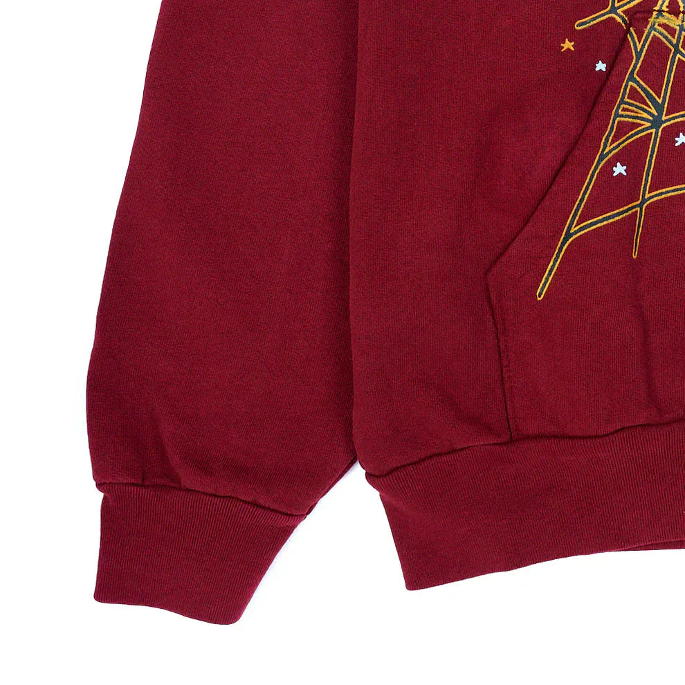 A close-up of the Burgundy Graphic Hoodie with Spider Web Print, a 440GSM heavyweight comfort fit pullover, showing the sleeve and hem with yellow and white embroidered geometric and star details.