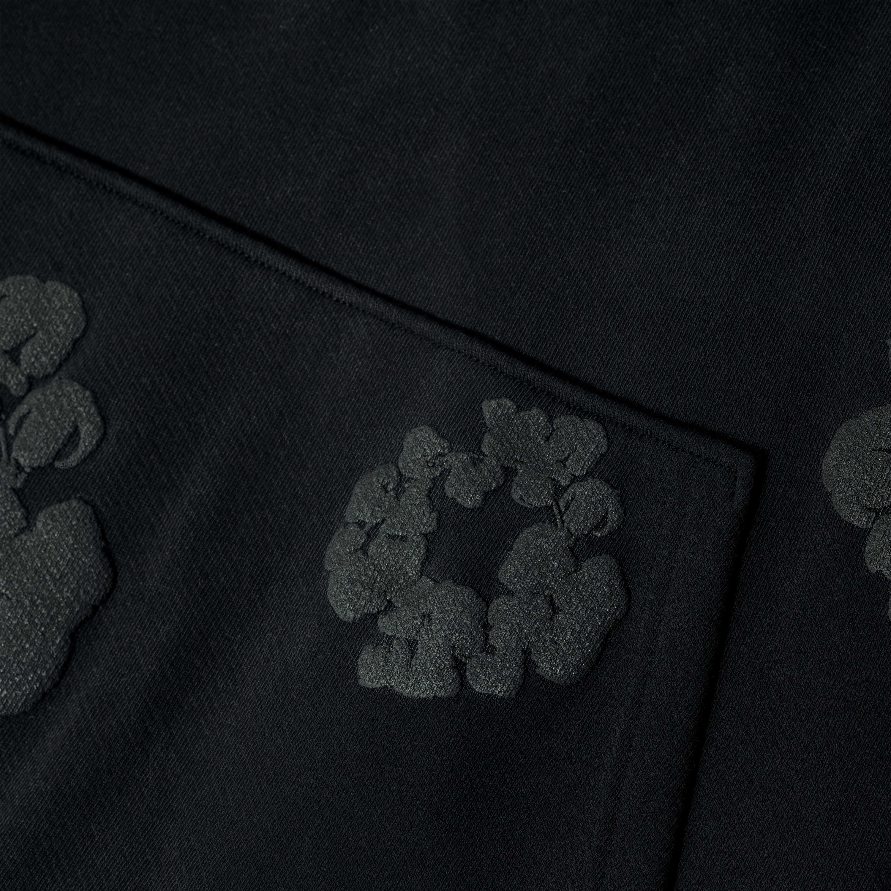 A close-up of the Black Monochrome “Cotton Wreath” Denim Tears Hoodie shows its raised floral pattern, a subtle textured detail ideal for streetwear fans or anyone seeking the hoodie’s signature cotton wreath motif.