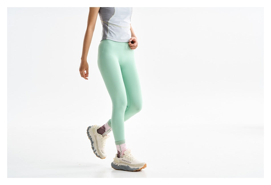 Cropped front view of mint leggings worn with a light gray top and striped socks.