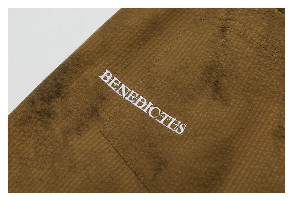 Close-up of white BENEDICTUS embroidery on the textured brown shorts fabric.