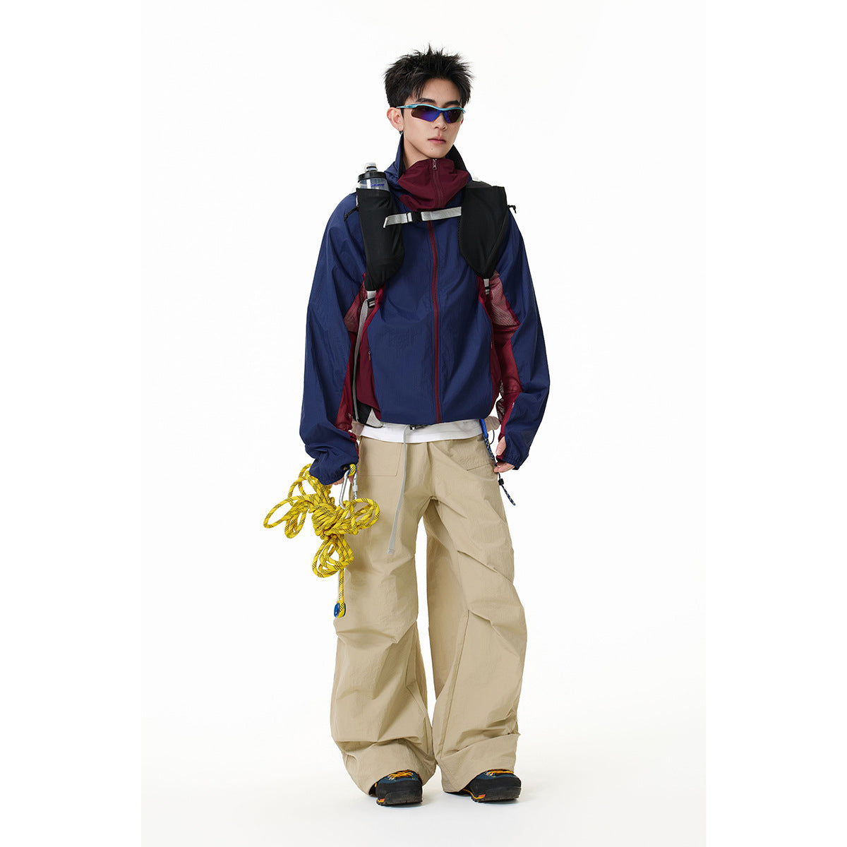 Model wearing a navy zip-up jacket with burgundy panels and a high collar, paired with loose beige trousers.