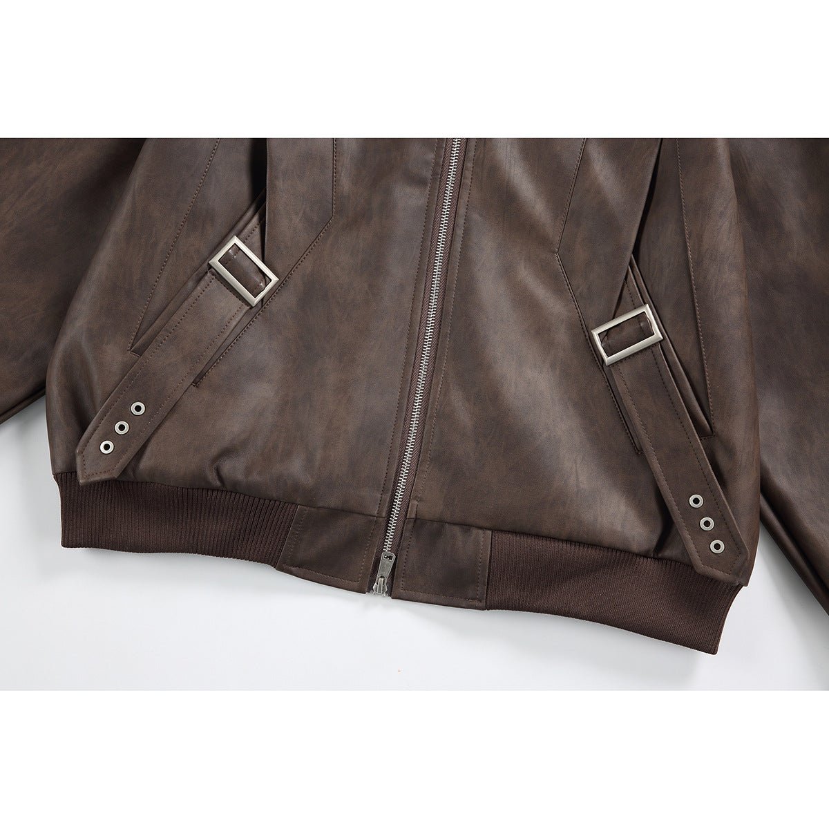 Close-up of the brown jacket's zip-front, ribbed hem, and adjustable pocket straps with metal buckles.