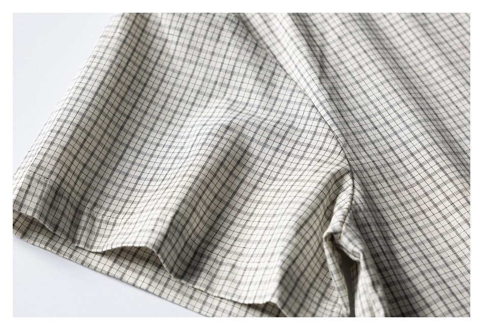 Close-up of the cream shirt's black-and-gray plaid fabric draped to show a seam and hem.