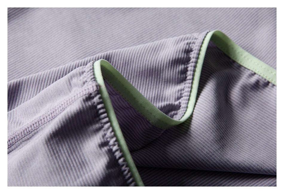 Close-up of a stitched edge on pale lavender-gray ribbed fabric, finished with pale green binding.