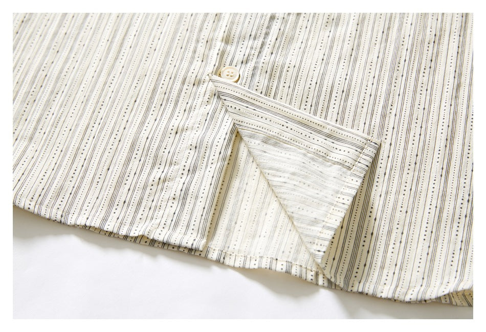 Close-up of a buttoned opening at the hem of an ivory garment with fine black vertical stripes and dots.