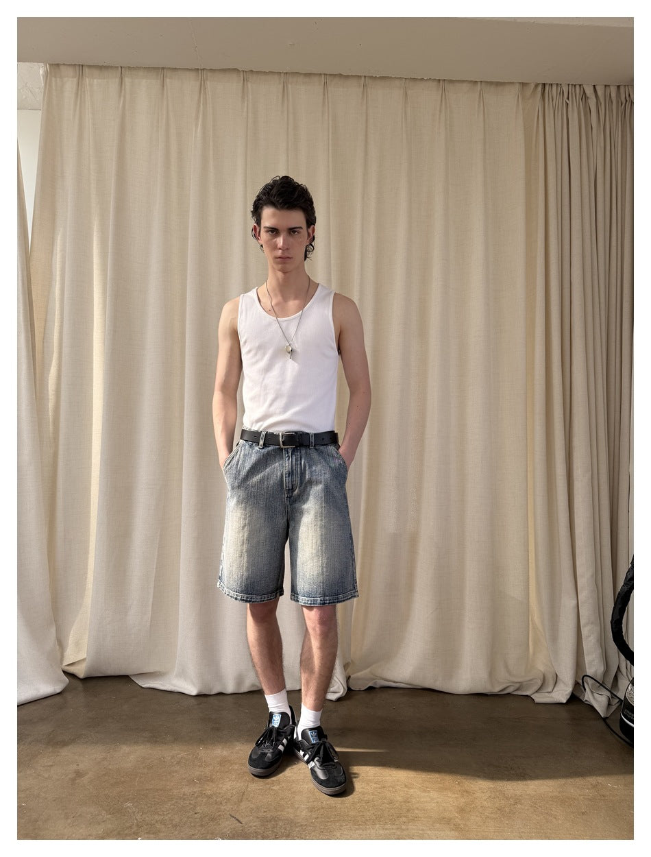 Model wearing faded blue denim shorts with a white tank top, black belt, white socks and black sneakers.