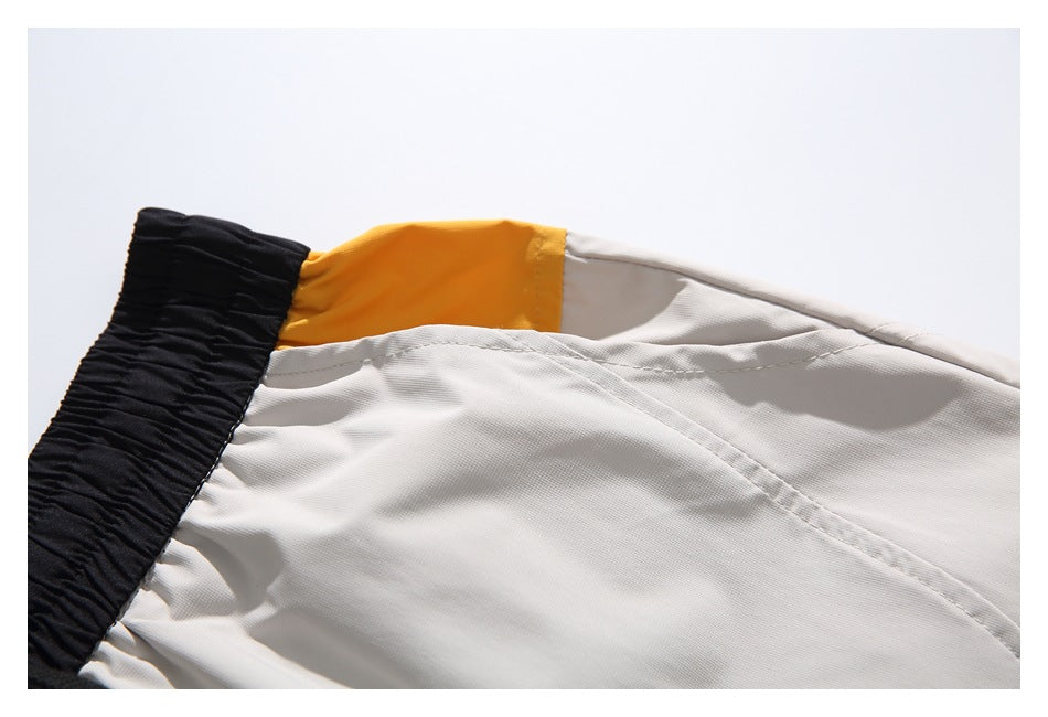 Close-up of a mustard-yellow panel and stitched seams on light gray shorts beside the black waistband.
