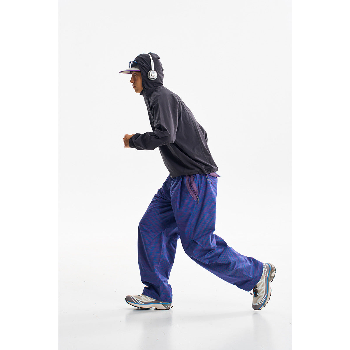 Person in a black hooded jacket and loose blue patterned pants, shown running in profile.