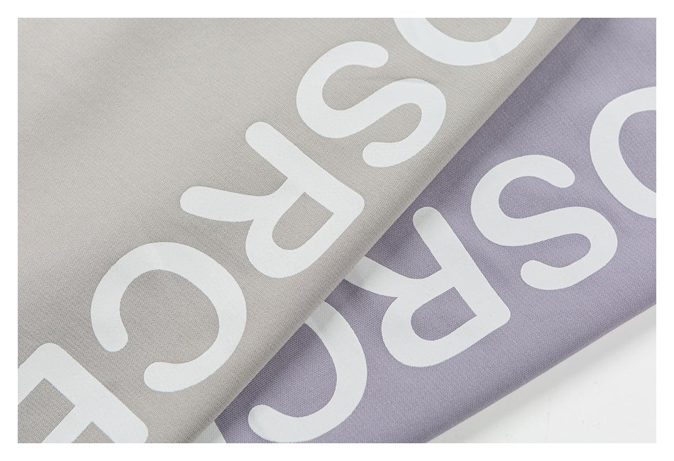 Close-up of large white lettering on overlapping light gray and lavender T-shirt fabric.