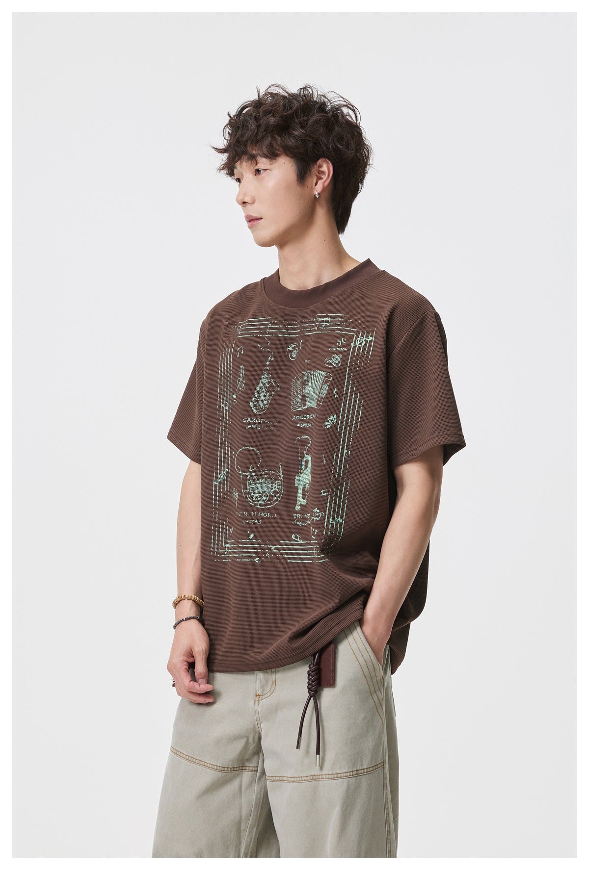 Angled front view of a model wearing a brown T-shirt with a large pale musical instrument graphic.