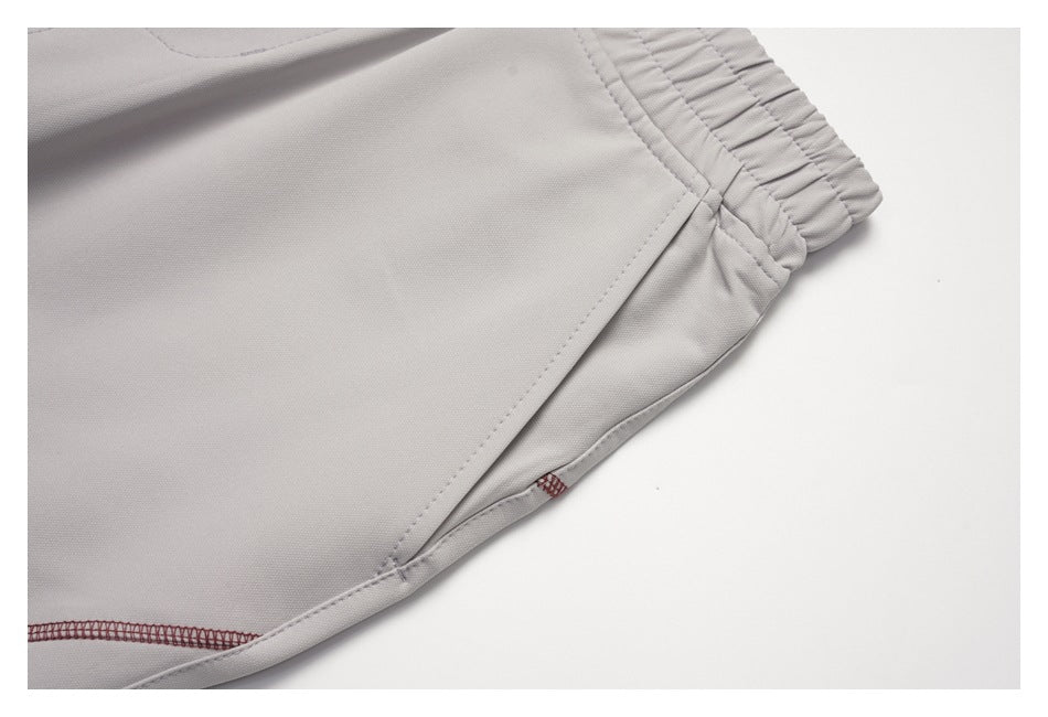 Close-up of light gray trousers showing the waistband, pocket stitching, and burgundy overlock seam.
