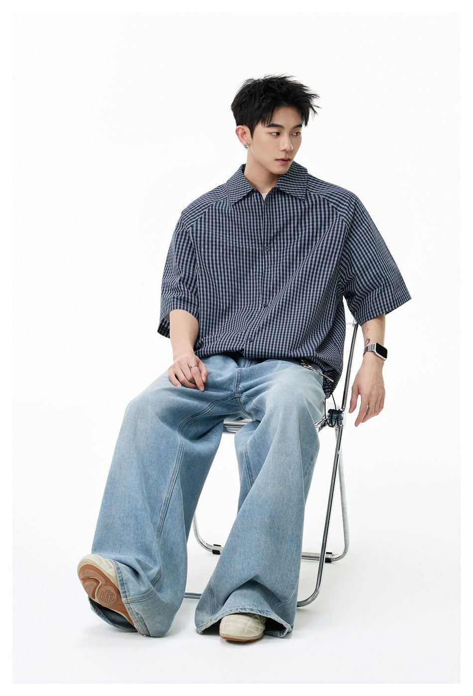 Seated model wearing a dark navy short-sleeve plaid shirt with light checks and an oversized fit.
