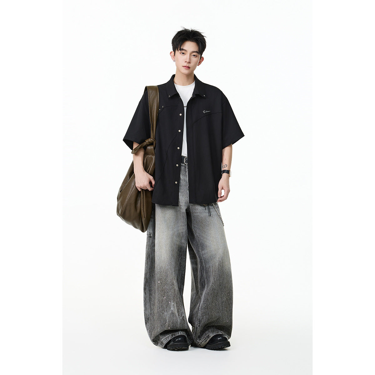 Model wearing a black short-sleeve button-up shirt with silver accents and oversized gray jeans.
