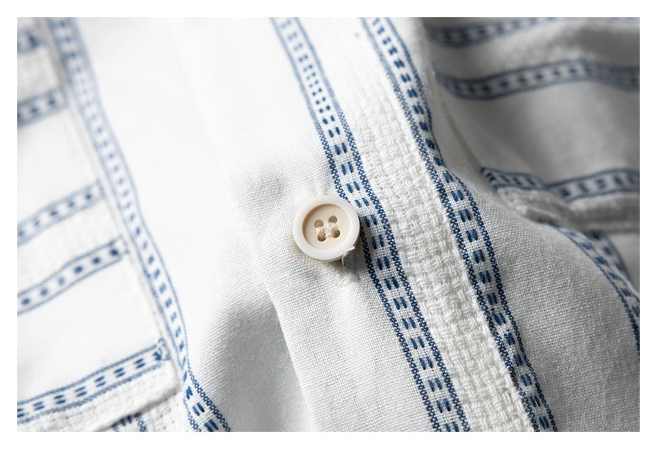 Close-up of a cream four-hole button on the placket of a white shirt with blue stripes.