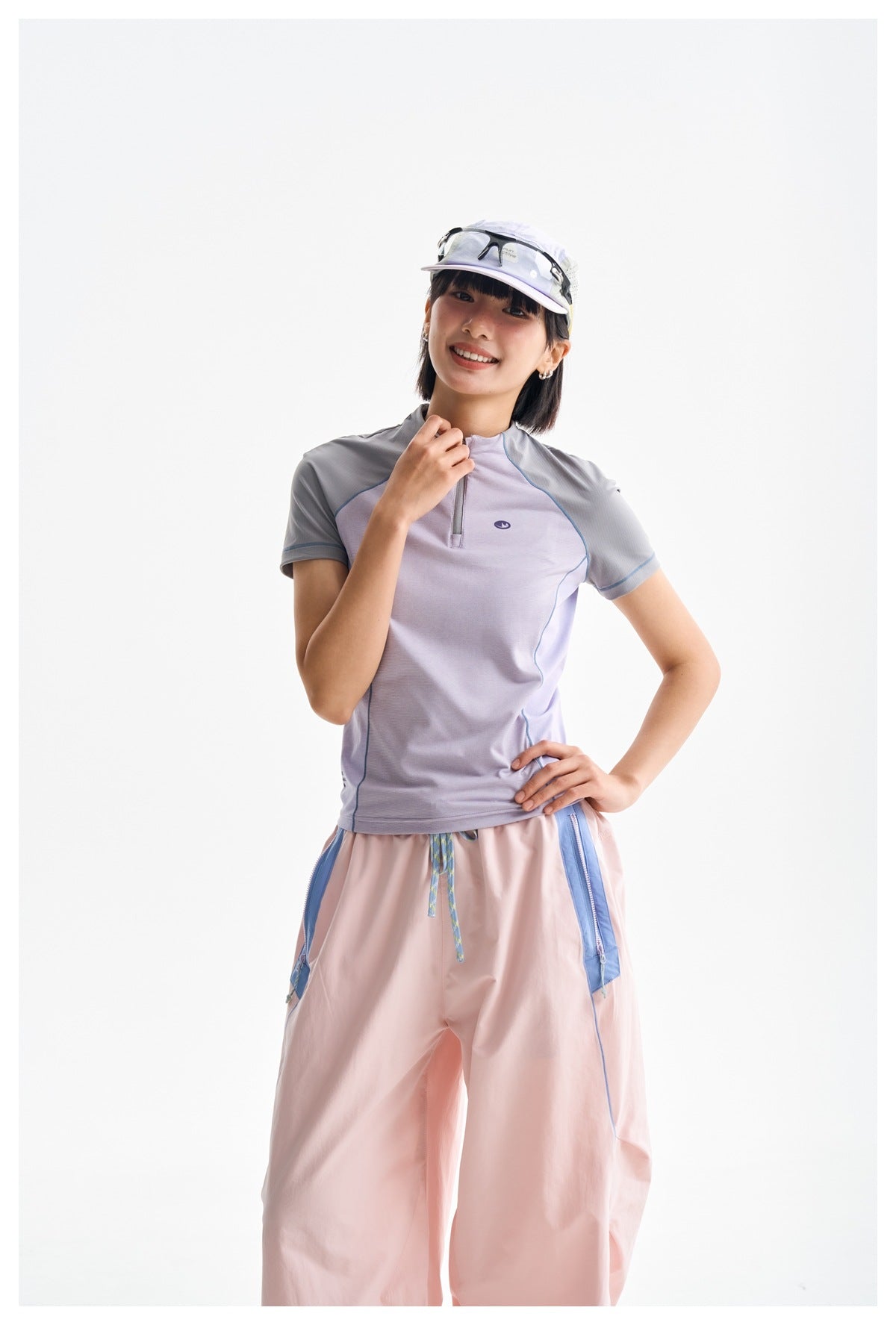 Model wearing a lavender and gray short-sleeve zip-neck top with loose pink trousers.