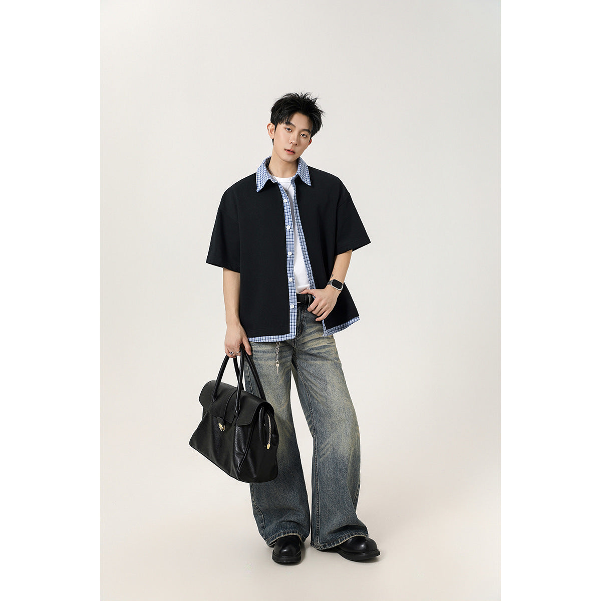 Model wearing a black short-sleeve button-up shirt with blue plaid collar, placket and hem trim.