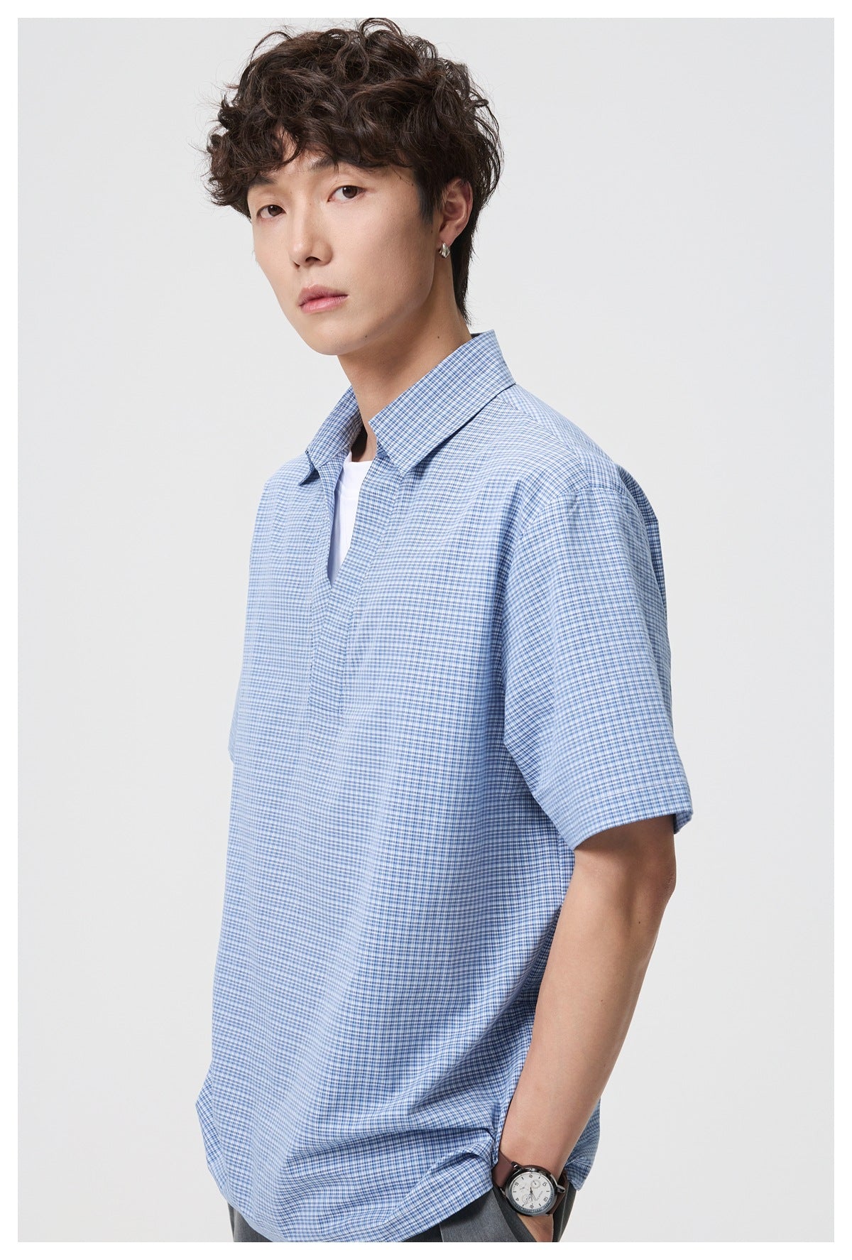 Model wearing a blue-and-white checked short-sleeve shirt with an open collar over a white T-shirt.