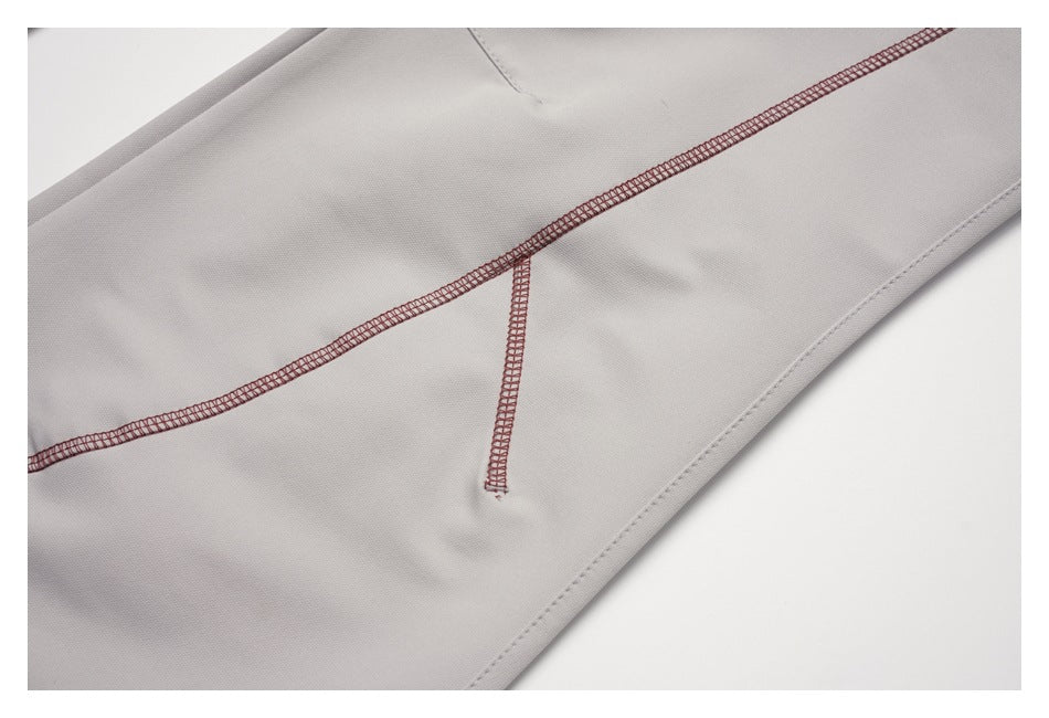 Close-up of light gray trouser fabric with burgundy overlock stitching and a finished edge.