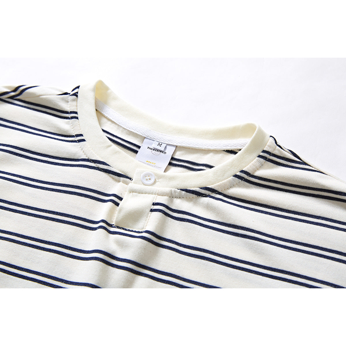 Close-up of an ivory T-shirt with navy horizontal stripes, showing its ribbed crew neck and single-button placket.