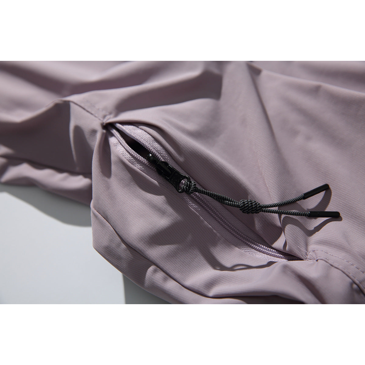 Close-up of a mauve shirt's side zipper pocket with a black cord pull.