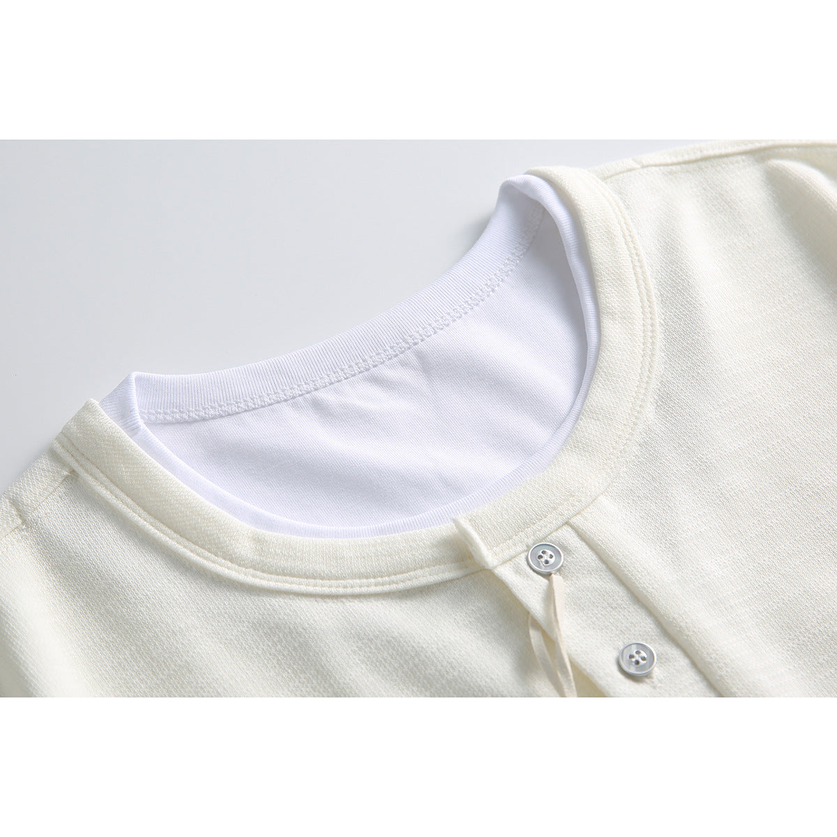 Close-up of an ivory short-sleeve henley shirt's ribbed crew neck and button placket.