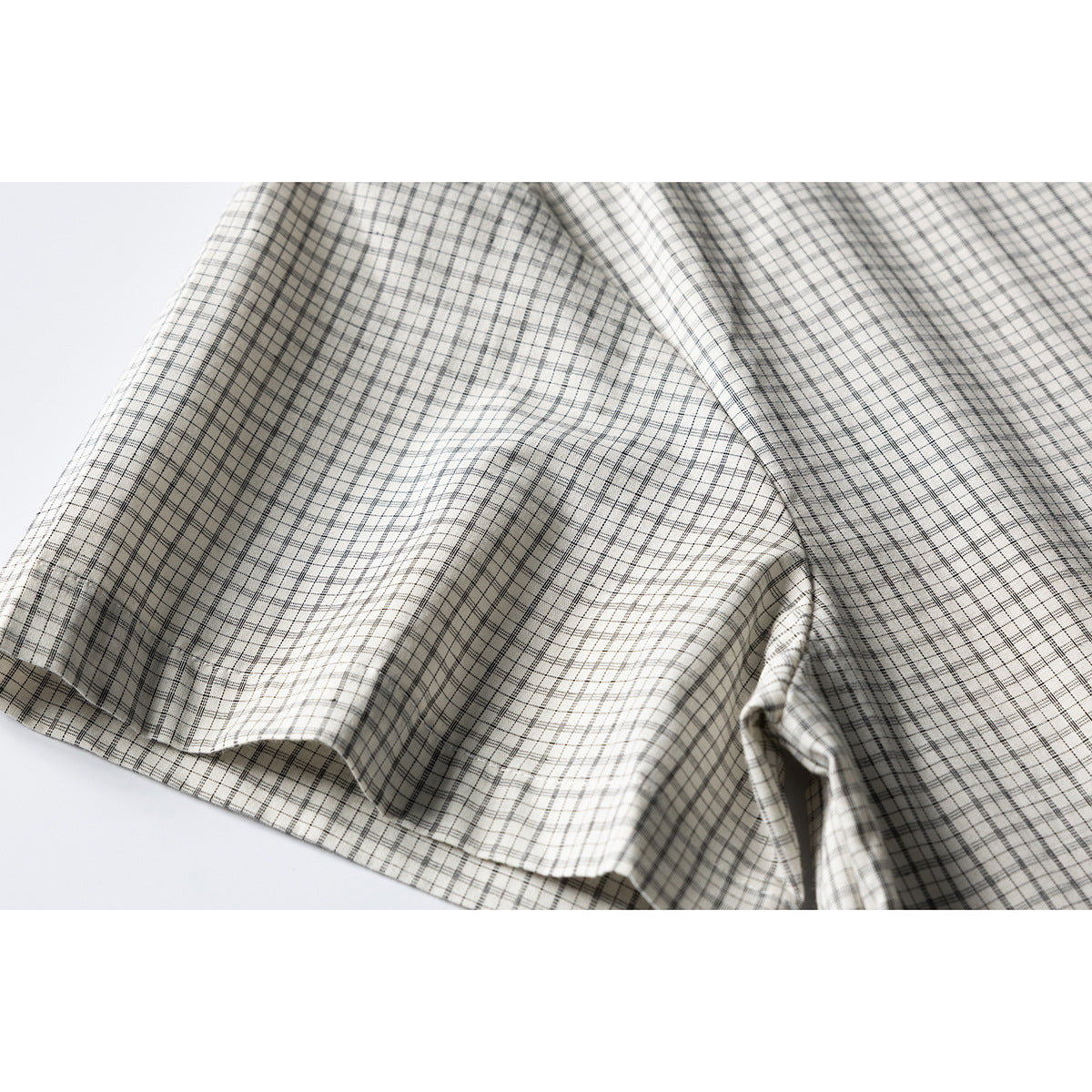 Close-up of the cream shirt's black-and-gray plaid fabric draped to show a seam and hem.