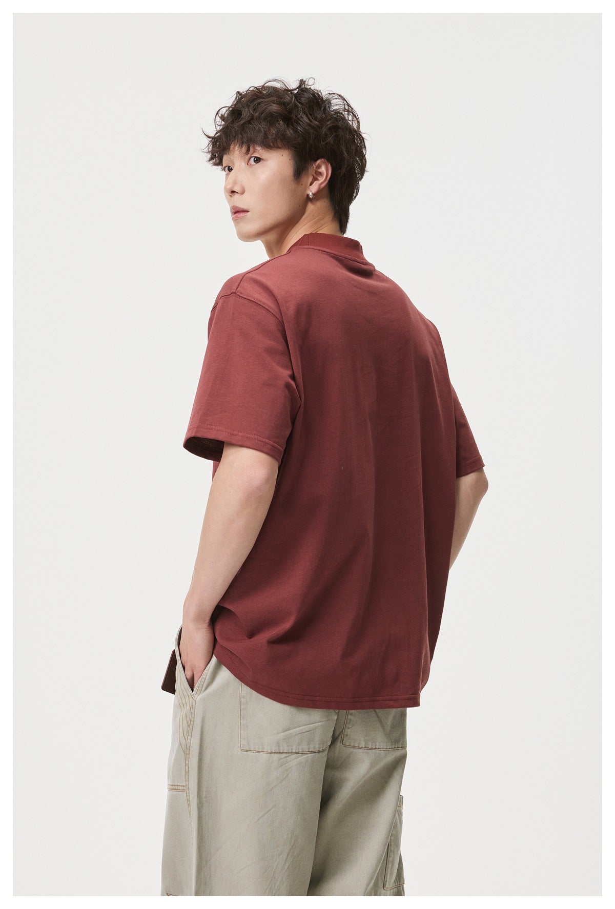 Rear three-quarter view of a model wearing a plain burgundy short-sleeve T-shirt with a high crew neck.