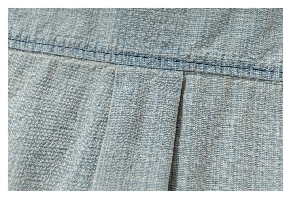 Close-up of a stitched seam and pleat on the light blue patterned shirt.