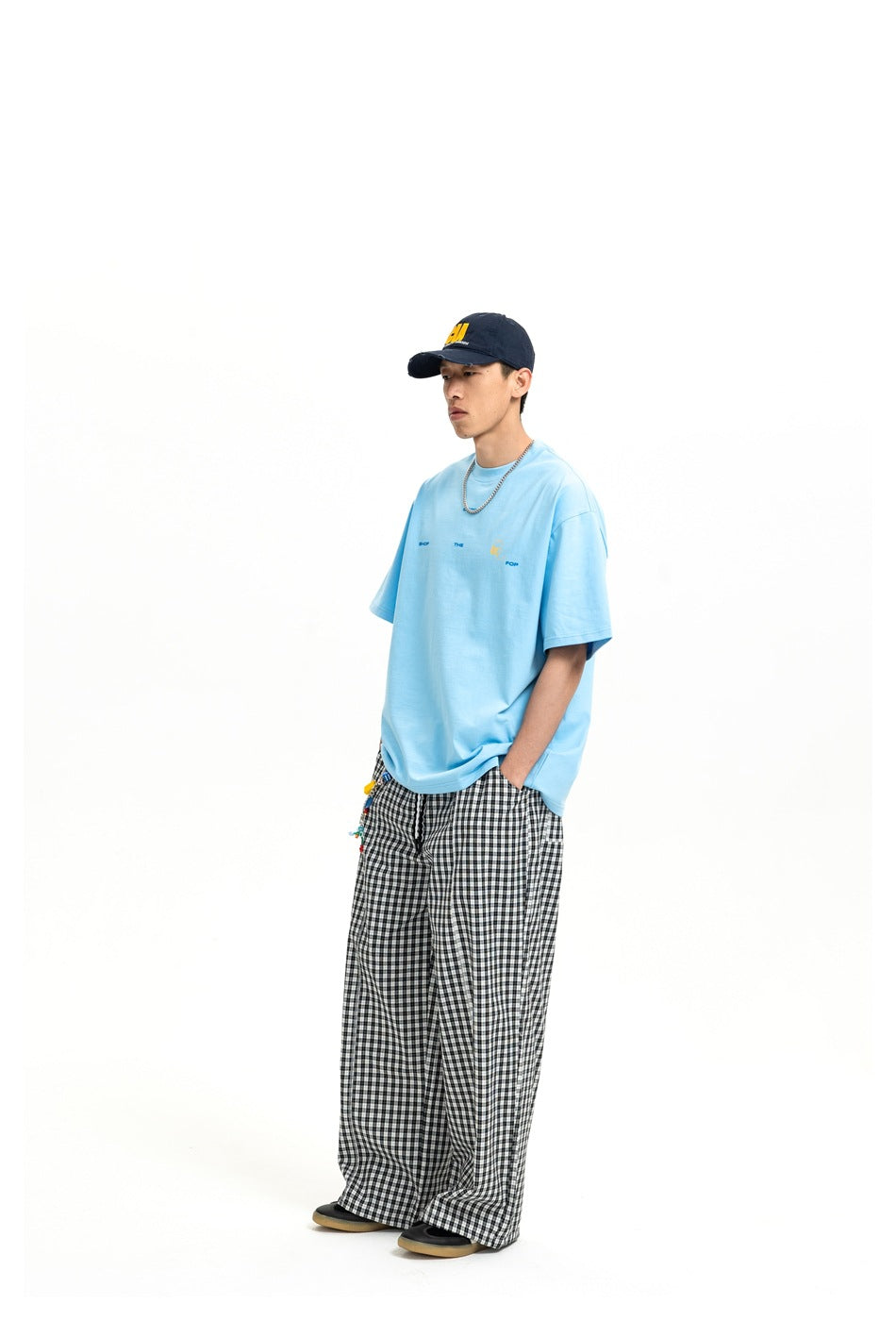Model wearing a light blue oversized T-shirt with black and white checked wide-leg pants and a navy cap, side view