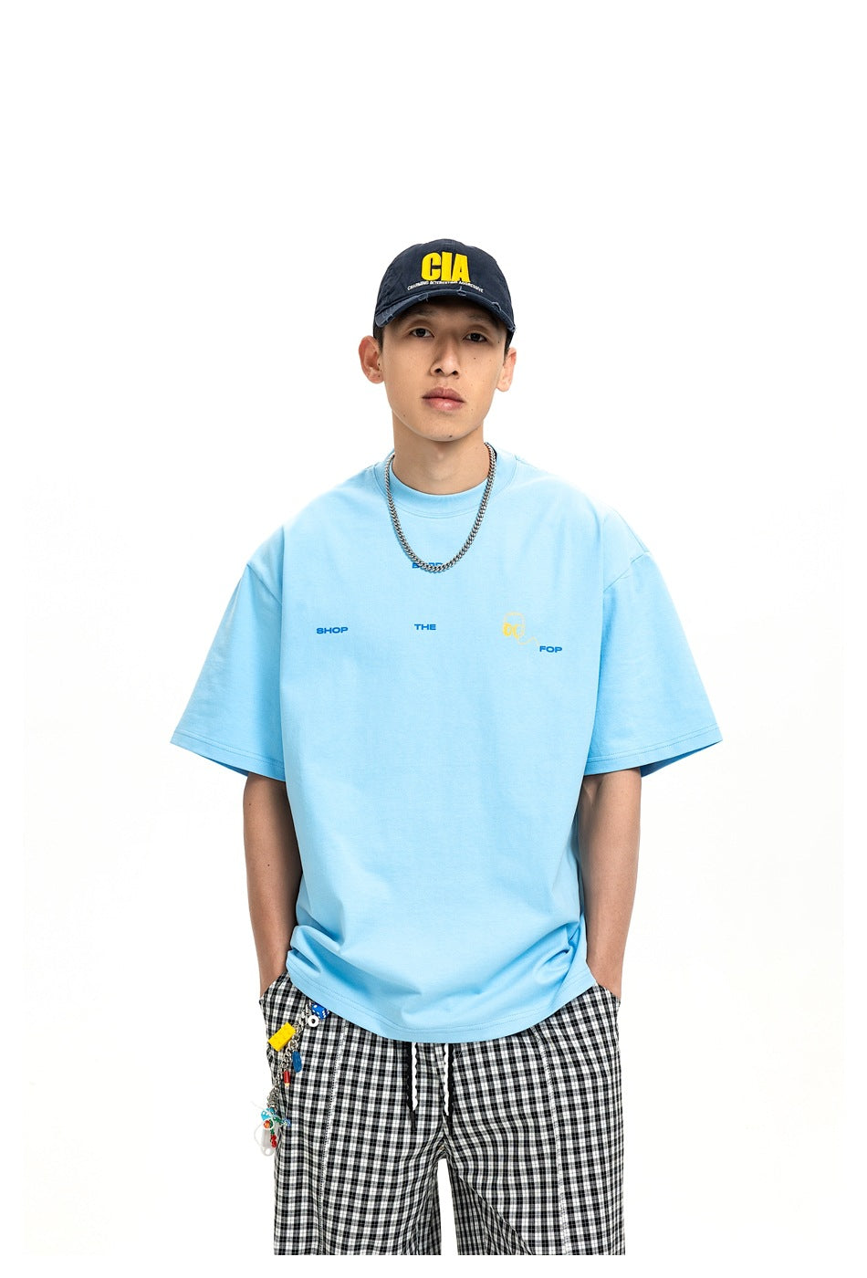 Model wearing an oversized light blue T-shirt with small chest graphics and black-and-white check trousers; front view.