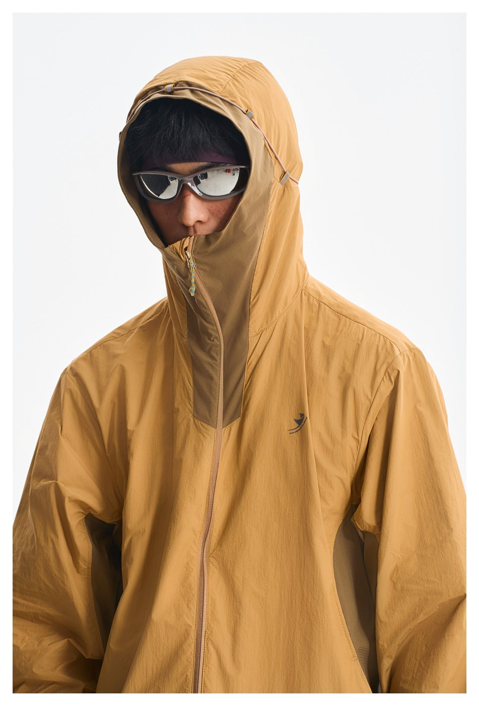 Close-up of a mustard hooded jacket with an adjustable hood, high zip collar, and small chest emblem.