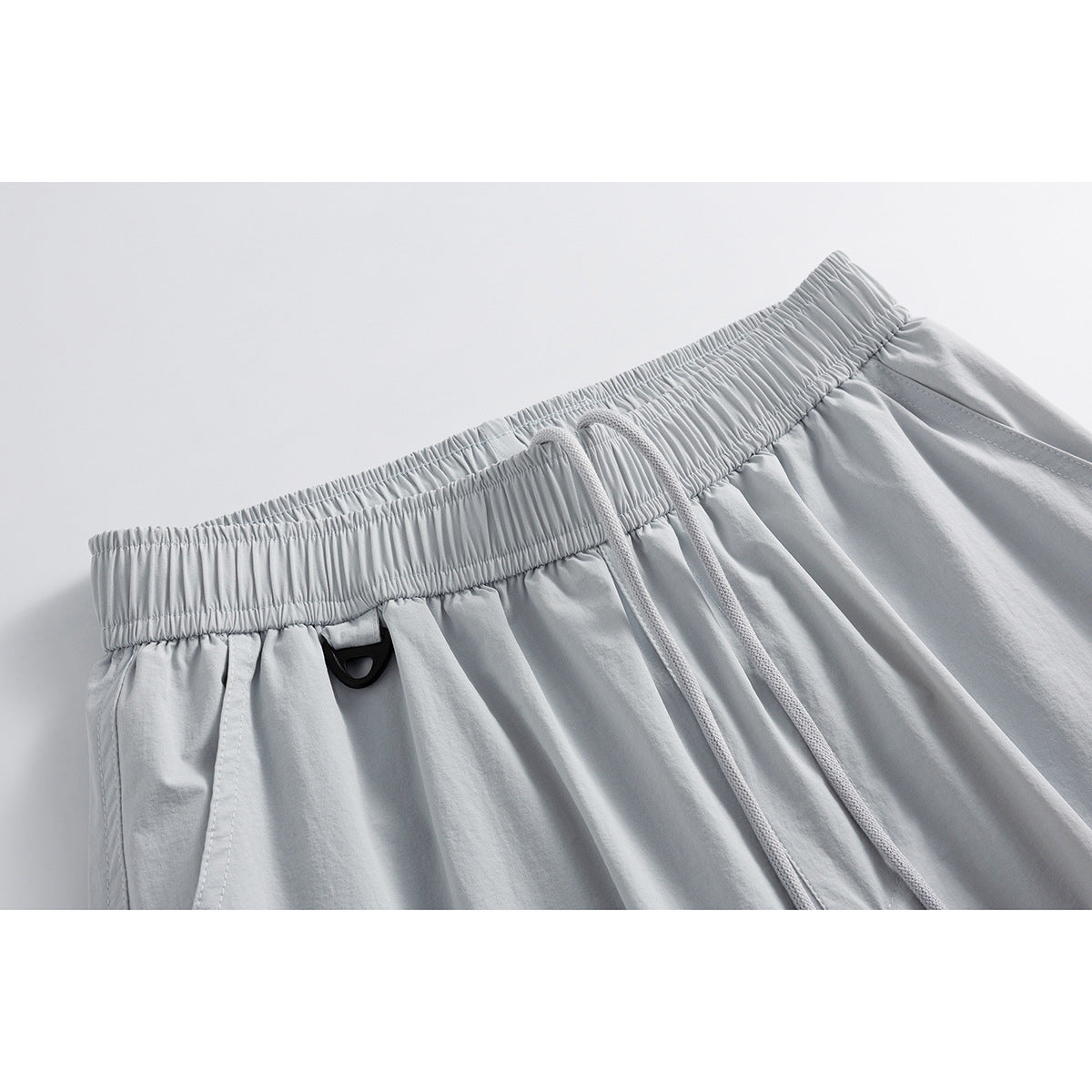 Close-up of light gray shorts showing a gathered elastic waistband, drawstring, and small black loop.