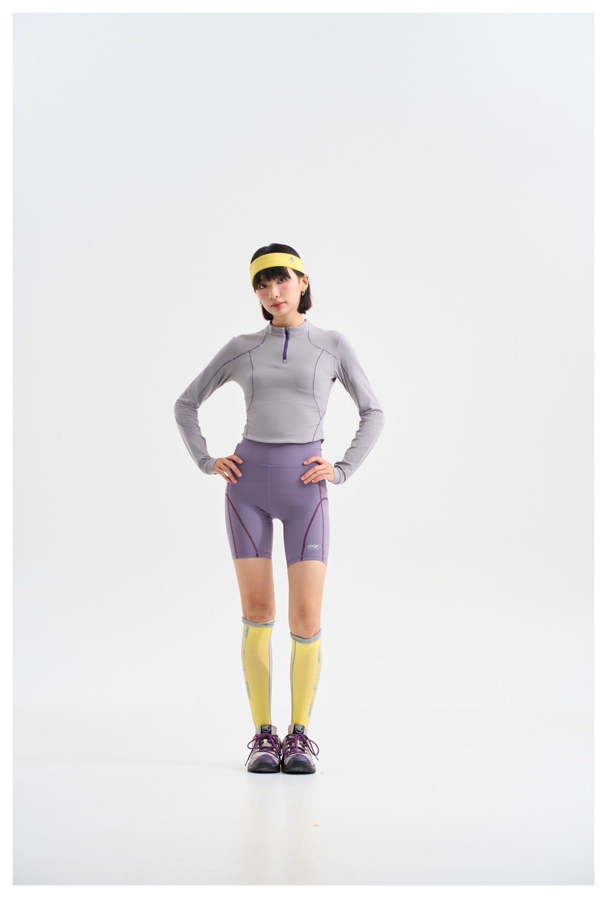Model wearing a light gray-lavender long-sleeve quarter-zip top, lavender cycling shorts, and yellow socks.