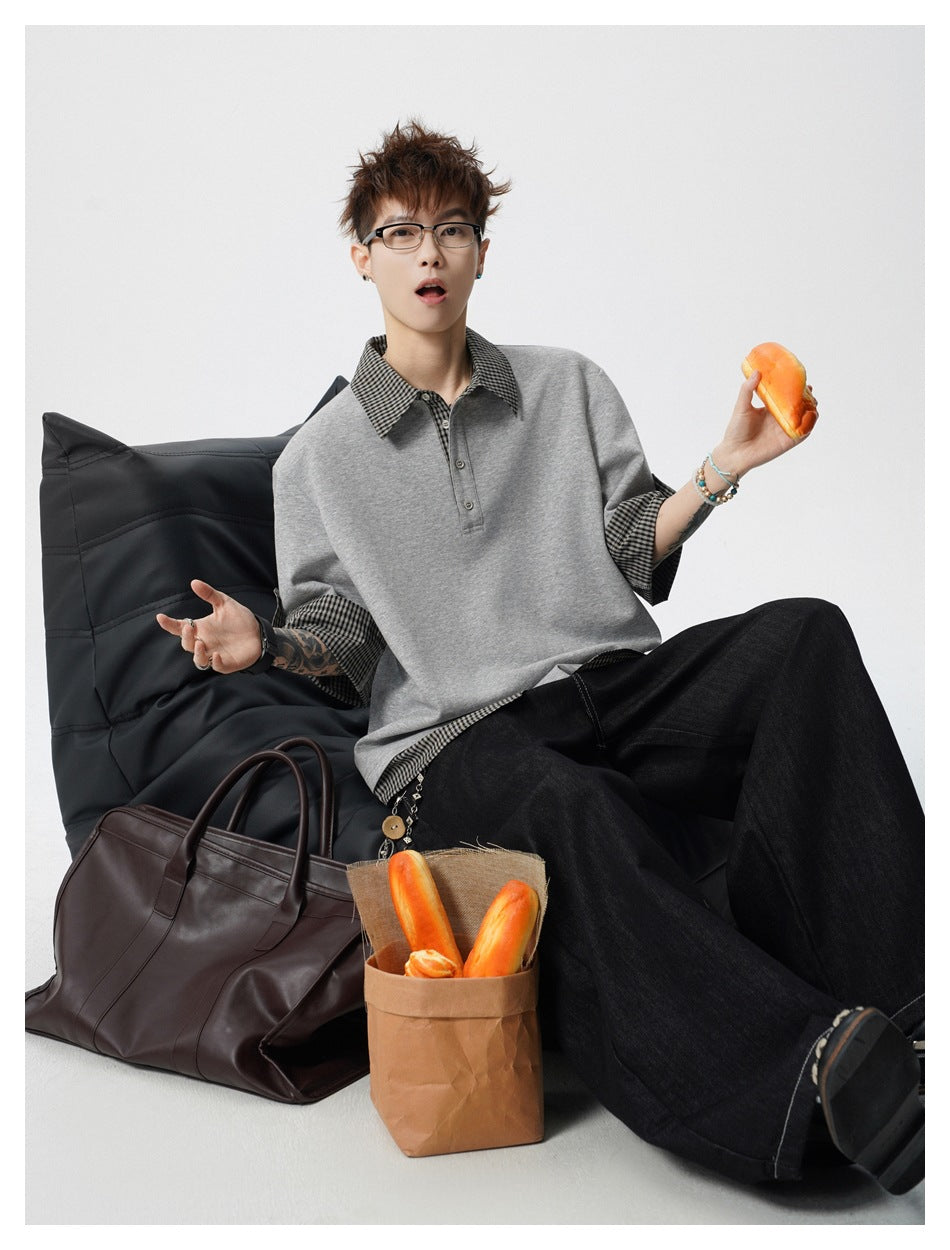 Seated model wearing an oversized gray top with checked collar and cuffs, styled with wide black trousers.