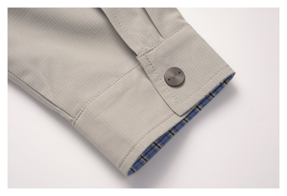 Close-up of a light taupe sleeve cuff with a dark button and blue plaid lining inside.