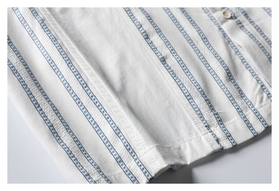 Close-up of a white shirt with narrow blue stripes, stitched seams and a small cream button.