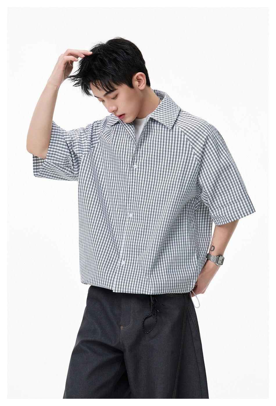 Model wearing a white short-sleeve button-up shirt with a fine black plaid pattern and adjustable hem.